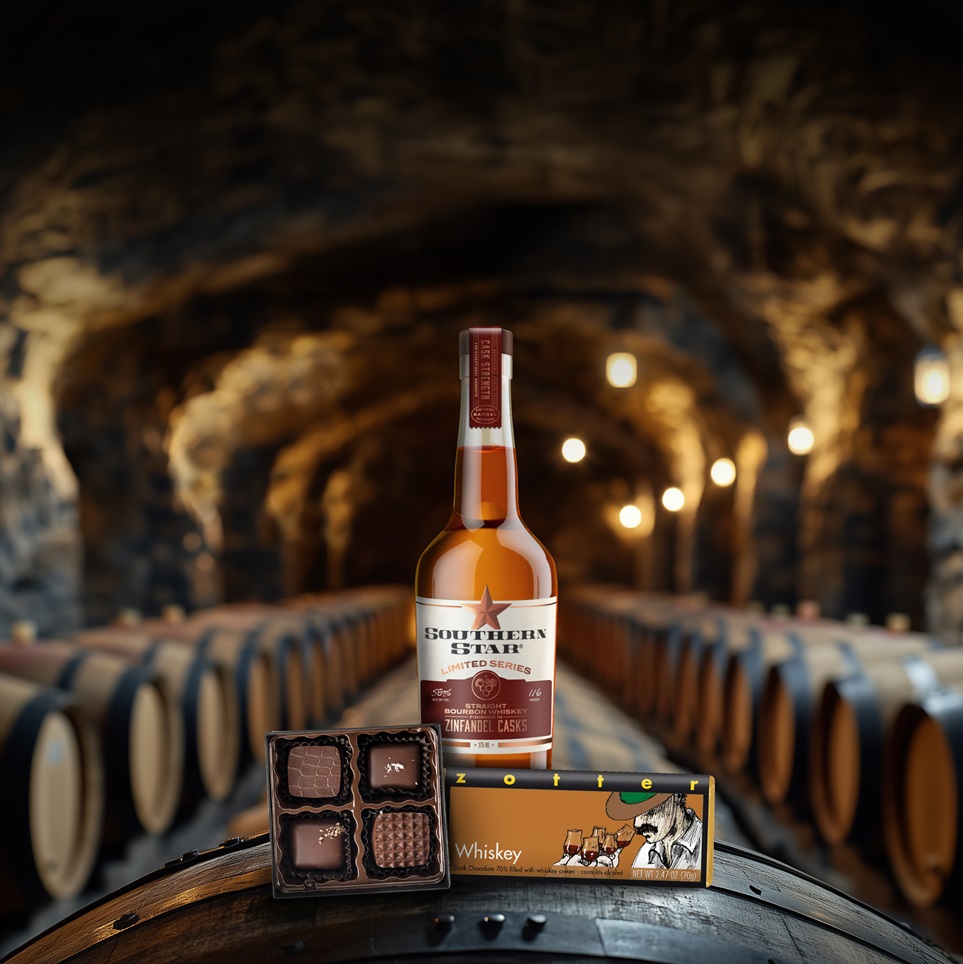 A bottle and glass of red wine rest on a barrel in a dimly lit w